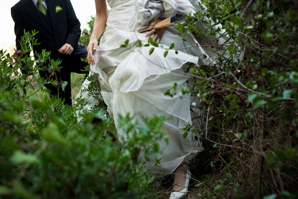 Legs of a woman in a wedding dress and a man in a suit, playfully running amidst tropical foliage.