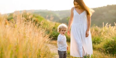 Mom and son in formal attire, holding hands and smiling while taking a portrait in the grass. Family photography capturing precious moments.