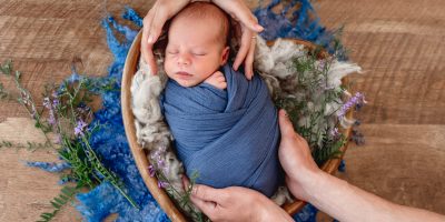 Newborn baby sleeps soundly in a blue bassinet, preparing for a comfortable and stress-free photography session.