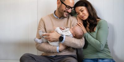 Happy parents embrace their newborn baby during a natural and authentic lifestyle photography session.