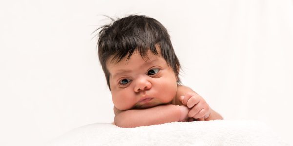 Newborn baby in white crib, peacefully posing for lifestyle photography session.