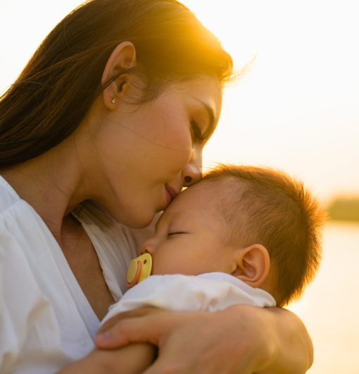 Loving mother holding and carrying her newborn baby with sunset view