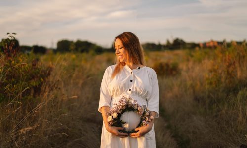 Portrait of a pregnant woman. A beautiful young pregnant woman in a white dress walks in the field.